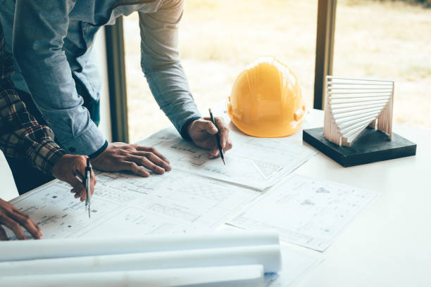 Two engineering man or co-workers working on a project and discussing together with looking at blueprint paperwork.